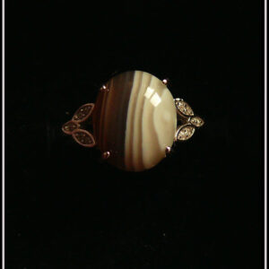 Bague avec un petit cabochon ovale en agate du Botswana, rayée de marron et de blanc montée sur un support en argent garni de chaque côté de trois petites mandorles contenant des éclats d'oxyde de zirconium Vue de dessus sur fond noir