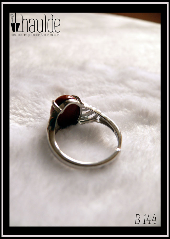 Bague avec un petit cabochon ovale en jaspe rouge montée sur un support en argent dont les côtés sont ajourés Vue de dos sur un fond blanc, l'anneau est réglable