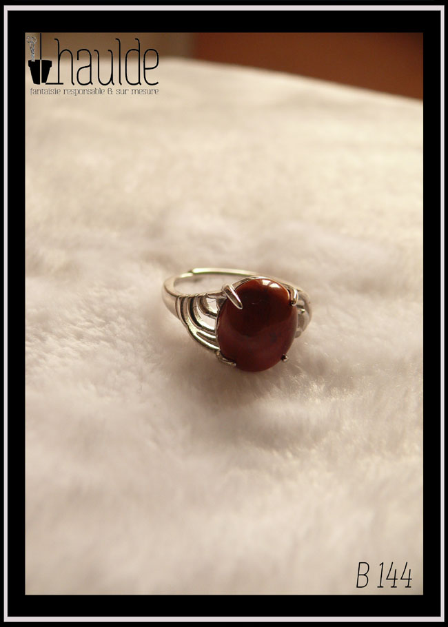 Bague avec un petit cabochon ovale en jaspe rouge montée sur un support en argent dont les côtés sont ajourés Vue de face sur un fond blanc, la pierre est opaque