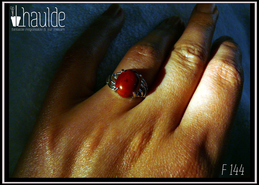 Bague avec un petit cabochon ovale en jaspe rouge montée sur un support en argent dont les côtés sont ajourés Vue portée sur un annulaire au soleil