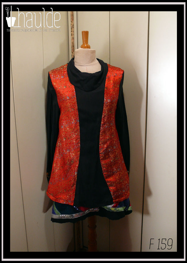 Tunique longue à manches longues. Centre, col, manches et dos en tencel noir. Manchettes brodées de perles et de miroirs. Côtés devant en soie synthétique rouge brocardée de motifs dorés Vue de face sur un mannequin de couture Avec la jupe "nanny core" en velours milleraies noires garnie de losanges de velours entourés de galons de sequins