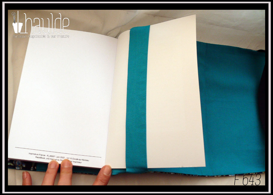 Vue du protège livre ouvert, côté bande intérieure dans laquelle est enfilé un livre. L'intérieur d'u protège livre est en tissu bleu cyan uni