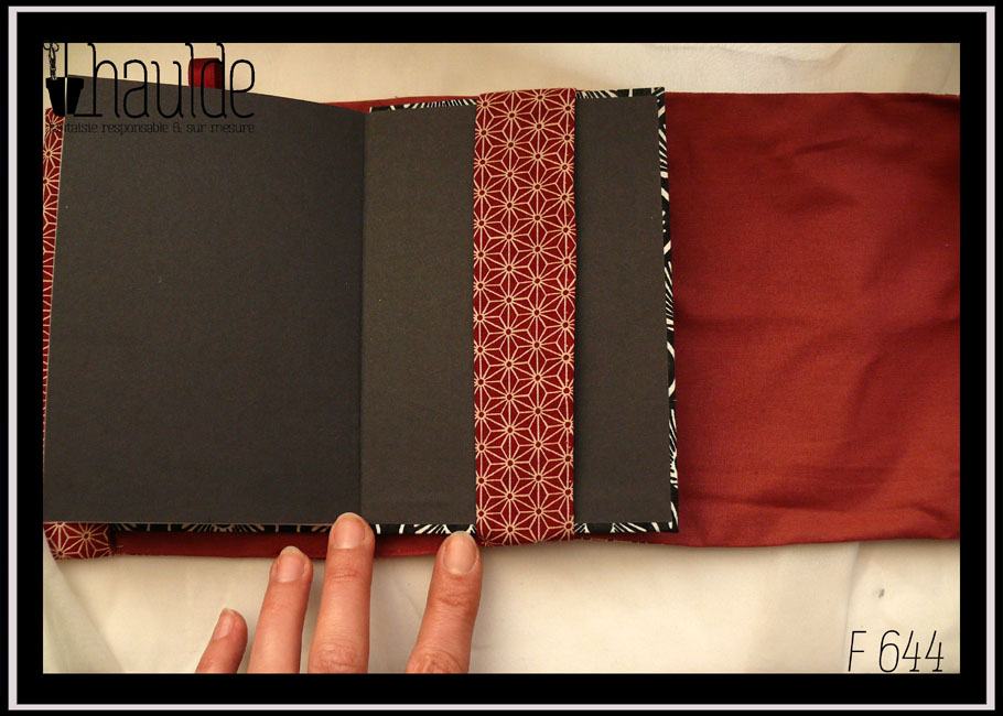 Protège livre en tissu rouge brique foncé imprimé de motifs géométriques japonais en étoile écrus Vu ouvert sur un carnet, côté bande de maintien L'intérieur du protège carnet est en tissu uni rouge brique
