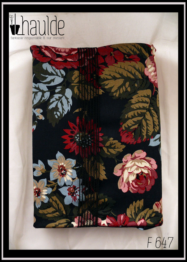 Protège livre en tissu noir imprimé hortensia s rouges foncés et blancs et autres fleurs dans les mêmes tons avec quelques fleurs et reflets bleus sur les feuillages Vu fermé par un gros élastique transparent rayé de noir