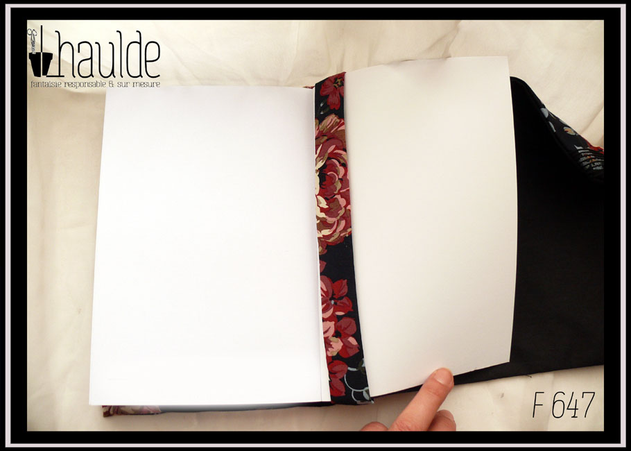 Protège livre en tissu noir imprimé hortensia rouges foncés et blancs Vu ouvert sur un livre, côté bande de maintien L'intérieur du protège livre est en tissu uni noir