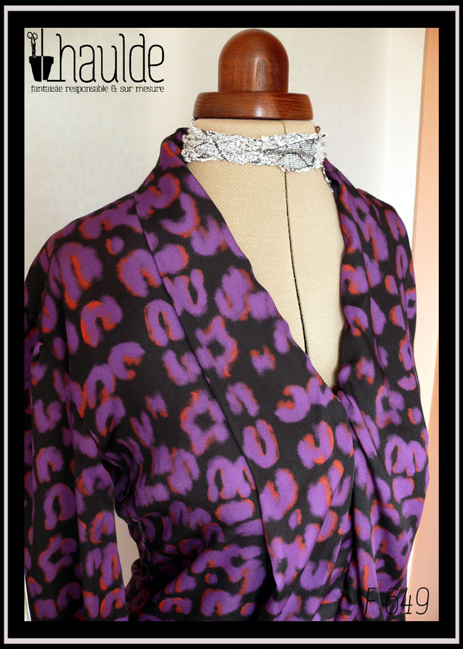 Chemisier à manches longues, col châle qui descend jusqu'en bas, vu de trois quarts face en plan rapproché, en tissu fluide noir imprimé motif panthère stylisé violet légèrement souligné de orange
