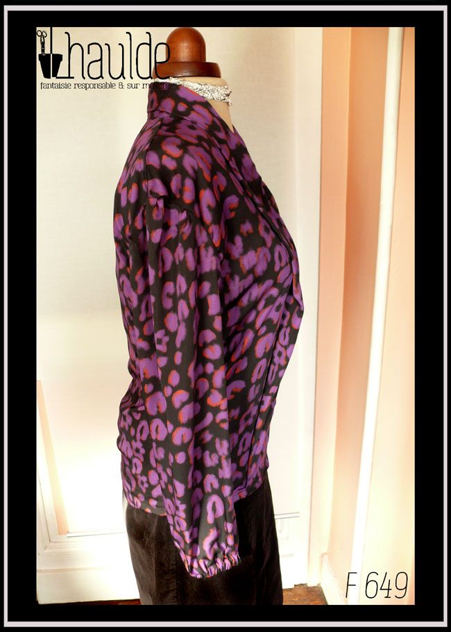 Chemisier à manches longues, col châle qui descend jusqu'en bas, vu de profil, en tissu fluide noir imprimé motif panthère stylisé violet légèrement souligné de orange