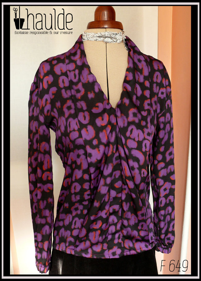 Chemisier à manches longues, col châle qui descend jusqu'en bas vu de face en tissu fluide noir imprimé motif panthère stylisé violet légèrement souligné de orange