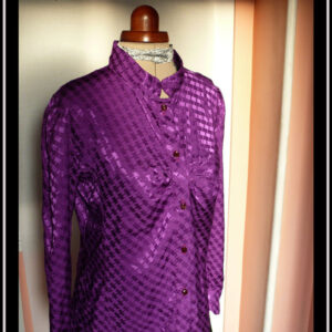 Chemisier à manches longues, col officier incliné vers le centre (peut se porter cassé) en jacquard de viscose, motif rectangles ondulés reliés par des lignes, comme le motif traditionnel dit "pied de poule" Légères fronces horizontales au niveau de la poitrine, vu de trois quarts face sur un mannequin de couture