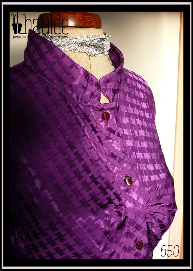 Chemisier à manches longues, col officier incliné vers le centre (peut se porter cassé) en jacquard de viscose, motif rectangles ondulés reliés par des lignes, comme le motif traditionnel dit "pied de poule" Légères fronces horizontales au niveau de la poitrine, vu en plan rapproché de trois quarts face sur un mannequin de couture