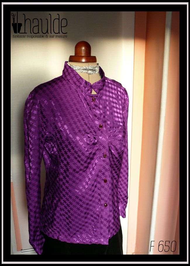 Chemisier à manches longues, col officier incliné vers le centre (peut se porter cassé) en jacquard de viscose, motif rectangles ondulés reliés par des lignes, comme le motif traditionnel dit "pied de poule" Légères fronces horizontales au niveau de la poitrine, vu de trois quarts face sur un mannequin de couture