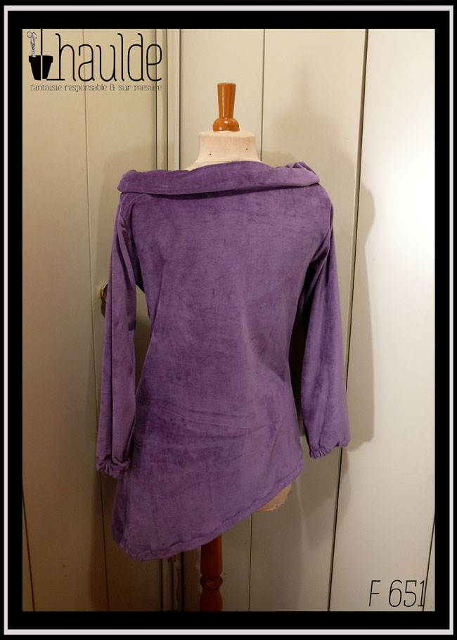 Haut manches longues, col bateau rabattu en velours mauve, vu de dos sur un mannequin de couture, le bas est asymétrique, il s'arrête au niveau des hanches à droite et descend 20 cm plus bas côté gauche
