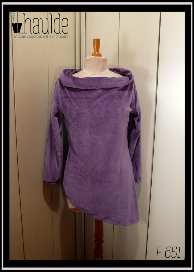 Haut manches longues, col bateau rabattu en velours mauve, vu de face sur un mannequin de couture, le bas est asymétrique, il s'arrête au niveau des hanches à droite et descend 20 cm plus bas côté gauche