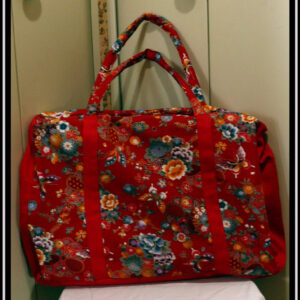 Grand sac en toile à anse. Tissu rouge imprimé pivoines et autres fleurs multicolores soulignées de dorées, d'inspiration nippone, petits côtés, dessous et bandes de renfort en sergé rouge Vu de face posé sur un guéridon