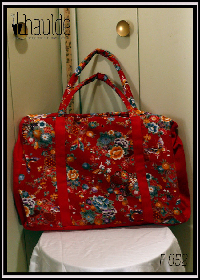 Grand sac en toile à anse. Tissu rouge imprimé pivoines et autres fleurs multicolores soulignées de dorées, d'inspiration nippone, petits côtés, dessous et bandes de renfort en sergé rouge Vu de face posé sur un guéridon