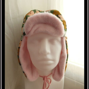 Chapka en jersey gratté imprimé, fleurs ocre, corail, écru et bleu pâle sur fond noir avec feuilles vertes stylisées, doublé de doudou rose pâle Vue de face sur une tête de mannequin