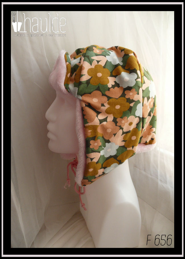 Chapka en jersey gratté imprimé, fleurs ocre, corail, écru et bleu pâle sur fond noir avec feuilles vertes stylisées, doublé de doudou rose pâle Vue de profil sur une tête de mannequin
