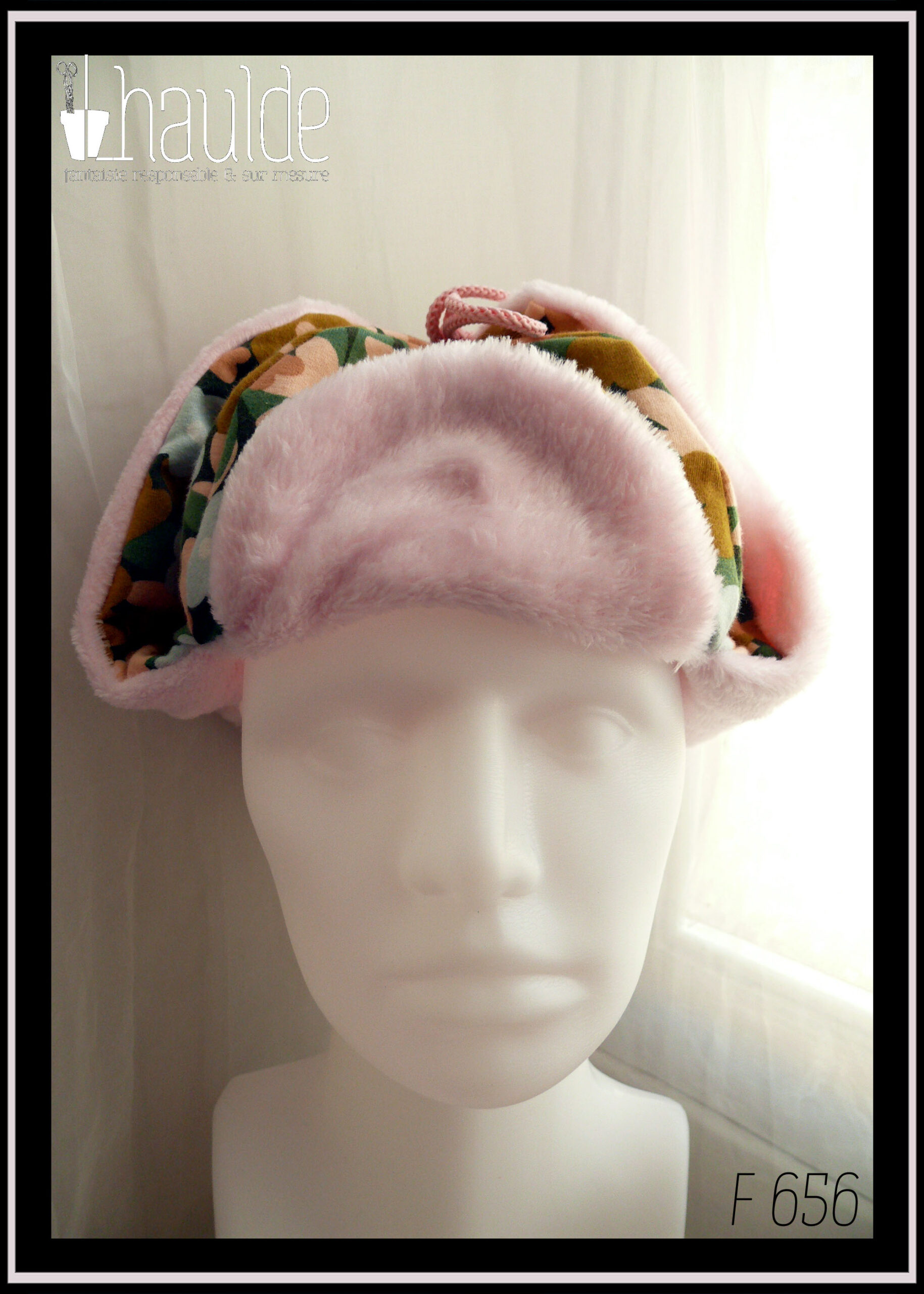 Chapka en jersey gratté imprimé, fleurs ocre, corail, écru et bleu pâle sur fond noir avec feuilles vertes stylisées, doublé de doudou rose pâle Vue avec les oreilles relevées sur une tête de mannequin