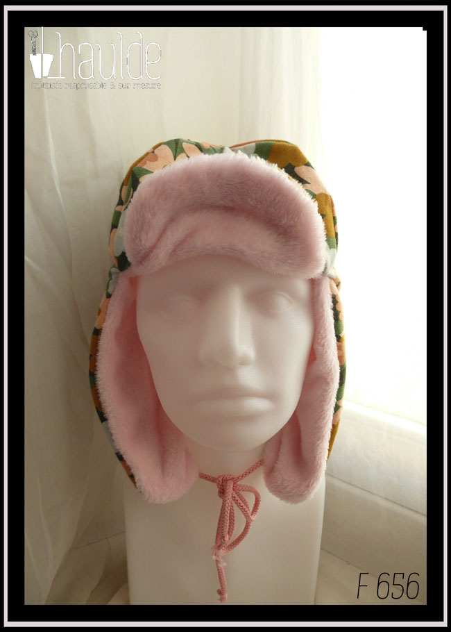 Chapka en jersey gratté imprimé, fleurs ocre, corail, écru et bleu pâle sur fond noir avec feuilles vertes stylisées, doublé de doudou rose pâle Vue de face sur une tête de mannequin