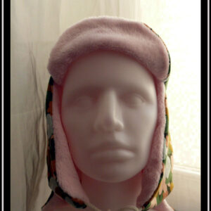 Chapka en jersey gratté imprimé, fleurs ocre, corail, écru et bleu pâle sur fond noir avec feuilles vertes stylisées, doublé de doudou rose pâle Vue de face sur une tête de mannequin