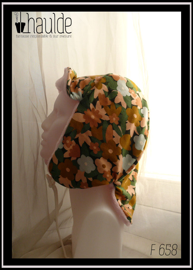 Chapka en jersey gratté imprimé, fleurs ocre, corail, écru et bleu pâle sur fond noir avec feuilles vertes stylisées, doublé de doudou rose pâle Vue de profil sur une tête de mannequin