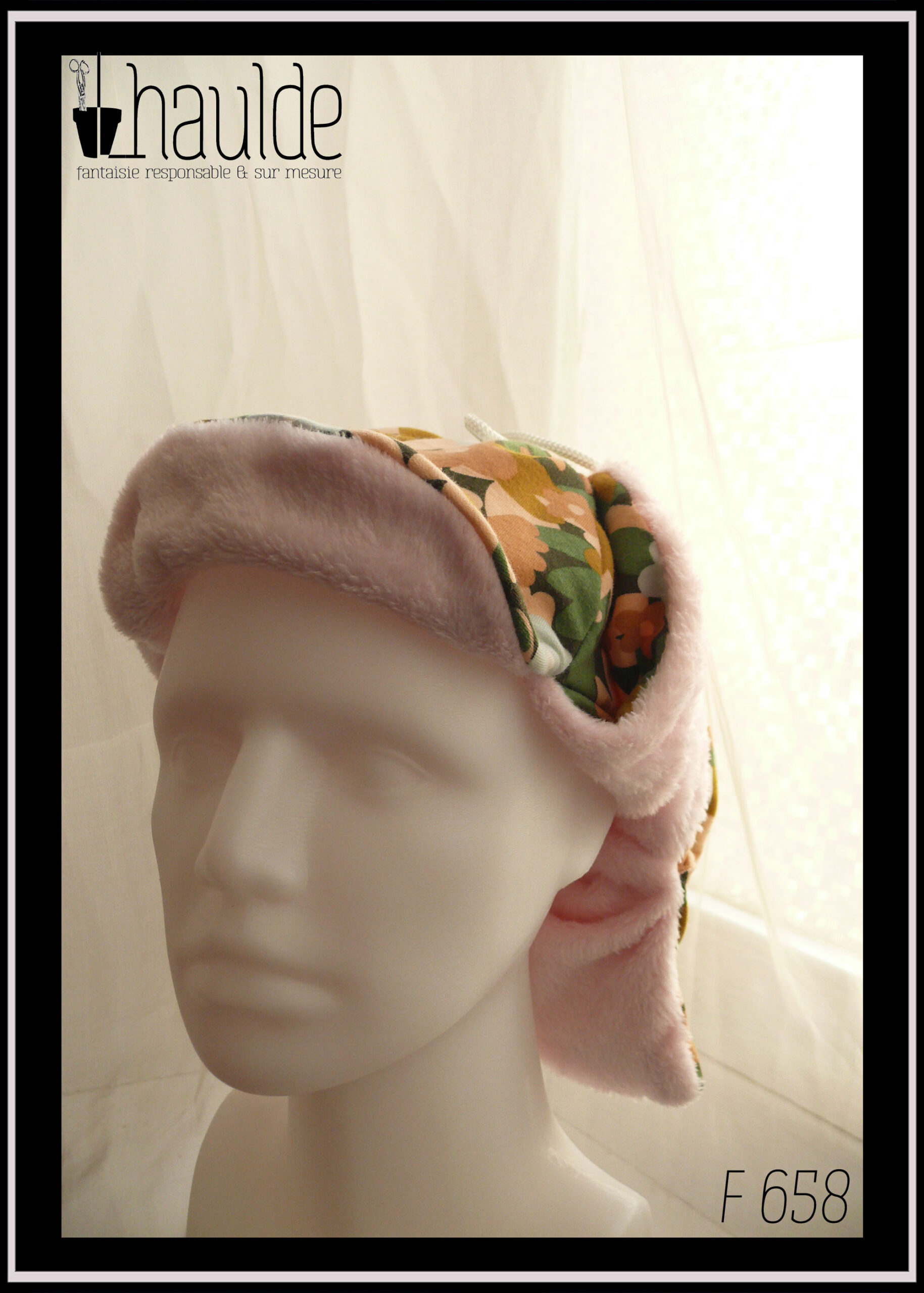 Chapka en jersey gratté imprimé, fleurs ocre, corail, écru et bleu pâle sur fond noir avec feuilles vertes stylisées, doublé de doudou rose pâle Vue avec oreilles relevées sur une tête de mannequin