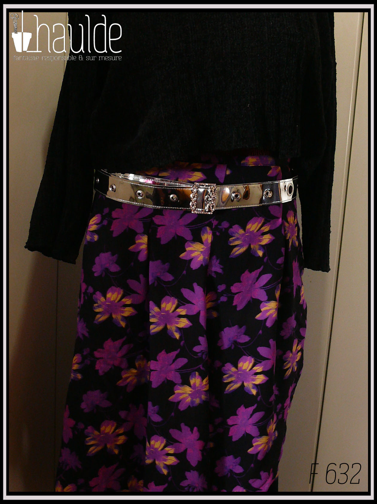 Une ceinture en simili cuir argenté rutilant avec une boucle rectangulaire décorée de strass Vue sur une jupe noire à fleurs violettes rehaussées de fuchsia et de jaune et un haut noir