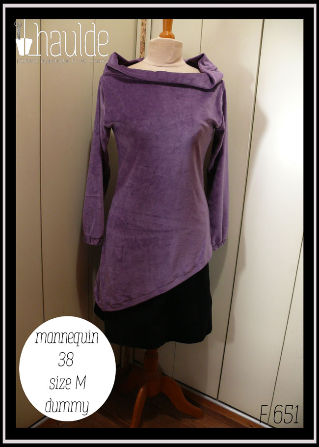 Haut manches longues, col bateau rabattu en velours mauve, vu de face sur un mannequin de couture, taille 38. Le bas est asymétrique, il s'arrête au niveau des hanches à droite et descend 20 cm plus bas côté gauche Le mannequin porte également une jupe courte noire