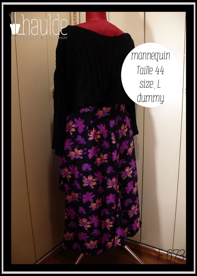 Jupe asymétrique en crêpe noir imprimé fleurs stylisées violet électrique, certaines ont des touches de jaune pâle ou de fuchsia fluo La jupe est très fendue et plus courte côté gauche, longue et très plissée dans le dos et côté droit. Vue de dos (long) sur un mannequin de couture taille 44 avec un pull noir