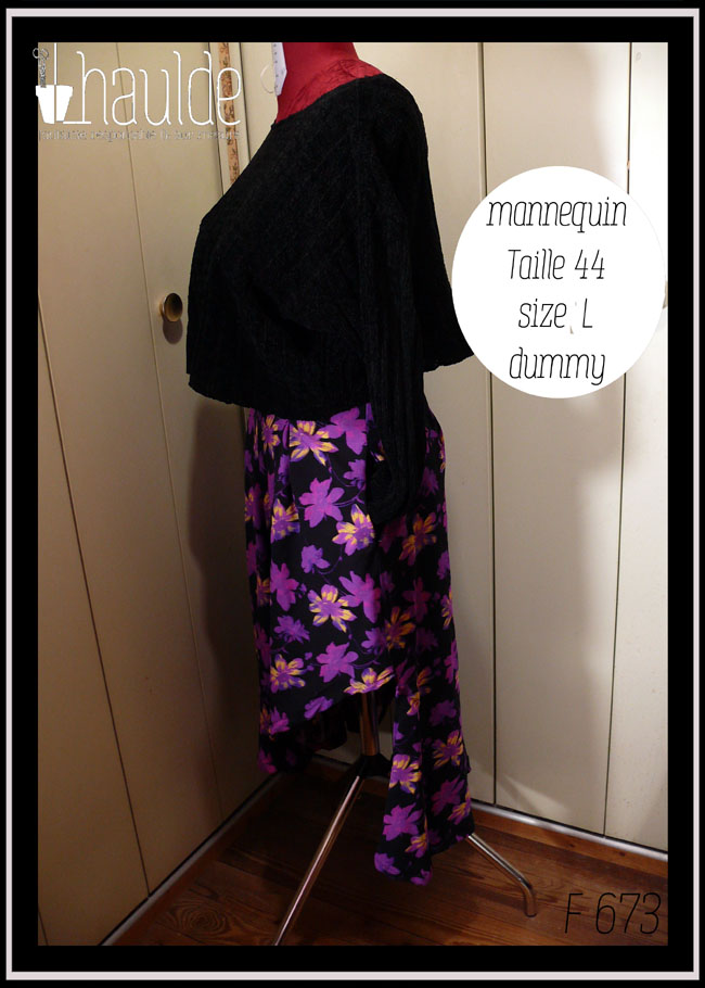 Jupe asymétrique en crêpe noir imprimé fleurs stylisées violet électrique, certaines ont des touches de jaune pâle ou de fuchsia fluo La jupe est très fendue et plus courte côté gauche, longue et très plissée dans le dos et côté droit. Vue de profil côté gauche (court) sur un mannequin de couture taille 44 avec un pull noir