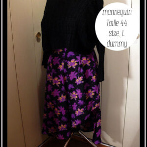 Jupe asymétrique en crêpe noir imprimé fleurs stylisées violet électrique, certaines ont des touches de jaune pâle ou de fuchsia fluo La jupe est très fendue et plus courte côté gauche, longue et très plissée dans le dos et côté droit. Vue de trois quarts gauche sur un mannequin de couture taille 44 et un pull noir