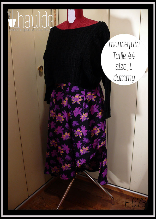 Jupe asymétrique en crêpe noir imprimé fleurs stylisées violet électrique, certaines ont des touches de jaune pâle ou de fuchsia fluo La jupe est très fendue et plus courte côté gauche, longue et très plissée dans le dos et côté droit. Vue de trois quarts gauche sur un mannequin de couture taille 44 et un pull noir