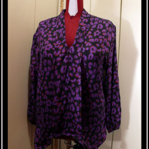 Chemisier à manches longues, col châle qui descend jusqu'en bas, vu de face sur un mannequin de couture, en tissu fluide noir imprimé motif panthère stylisé violet légèrement souligné de orange