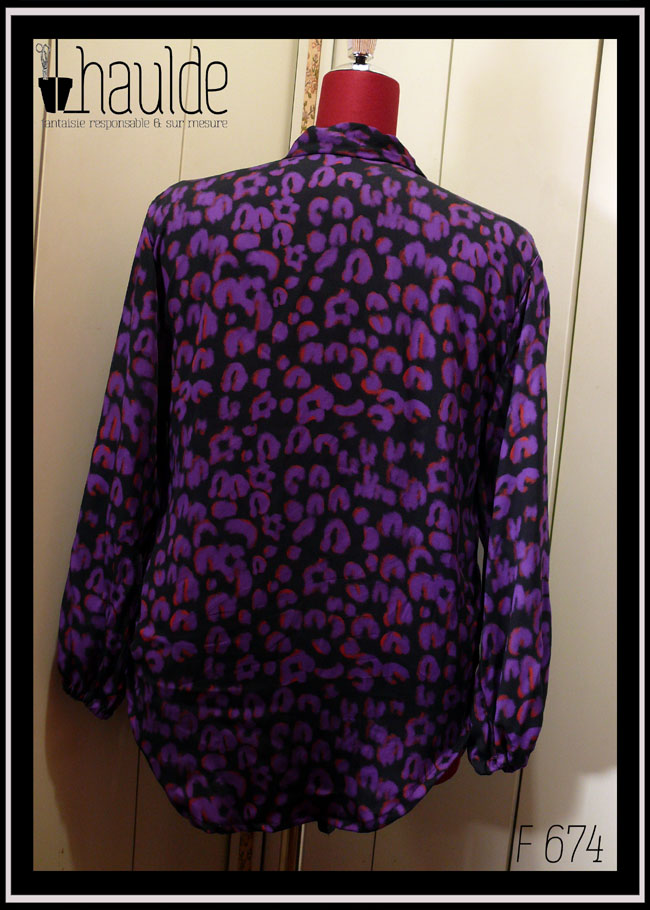 Chemisier à manches longues, col châle qui descend jusqu'en bas, vu de dos sur un mannequin de couture, en tissu fluide noir imprimé motif panthère stylisé violet légèrement souligné de orange