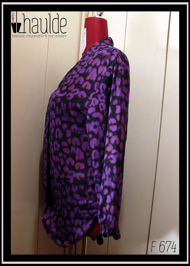 Chemisier à manches longues, col châle qui descend jusqu'en bas, vu de profil sur un mannequin de couture, en tissu fluide noir imprimé motif panthère stylisé violet légèrement souligné de orange