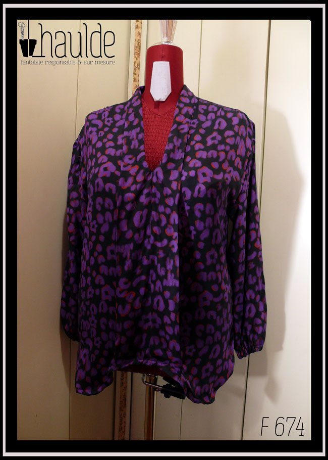 Chemisier à manches longues, col châle qui descend jusqu'en bas, vu de face sur un mannequin de couture, en tissu fluide noir imprimé motif panthère stylisé violet légèrement souligné de orange