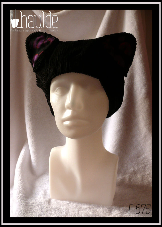 Bonnet en velours côtelé noir avec deux oreilles de chats dont l'intérieur est garni de tissu noir imprimé motifs panthère stylisé violet légèrement soulignés de orange Vu sur une tête de mannequin de trois quarts face