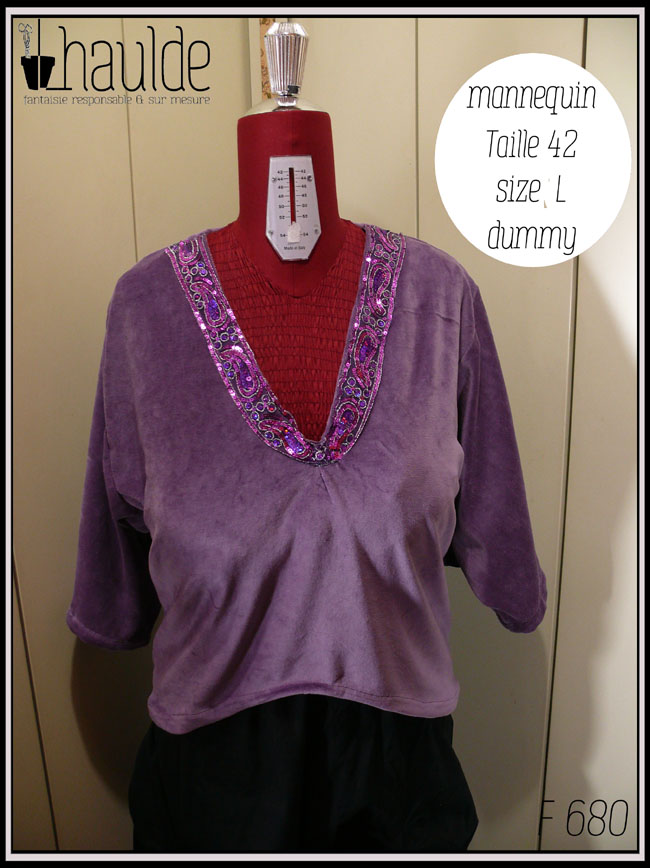 Haut col en V plongeant, manches kimono trois quarts en velours mauve. L'encolure est garnie d'un galon brodé de sequins violets et fuchsia qui forment des motifs paisley Vu sur un mannequin de couture taille 42