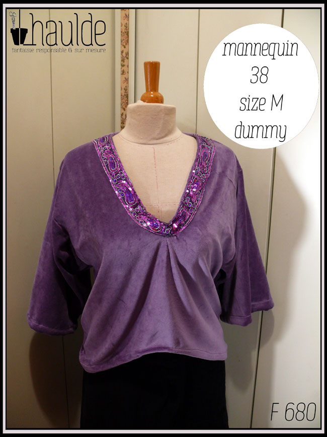 Haut col en V plongeant, manches kimono trois quarts en velours mauve. L'encolure est garnie d'un galon brodé de sequins violets et fuchsia qui forment des motifs paisley Vu sur un mannequin de couture taille 38