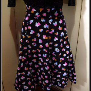 Jupe à ceinture large, pans évasés en velours milleraies noir imprimé de taches regroupées par trois ou quatre, mauve, vert pâle, ocre, rose et bleu, qui pourraient faire penser à un pelage animal (le motif s'appelle animal skin) Vue de face sur un mannequin de couture