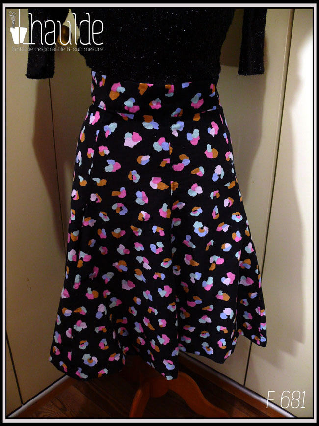 Jupe à ceinture large, pans évasés en velours milleraies noir imprimé de taches regroupées par trois ou quatre, mauve, vert pâle, ocre, rose et bleu, qui pourraient faire penser à un pelage animal (le motif s'appelle animal skin) Vue de face sur un mannequin de couture