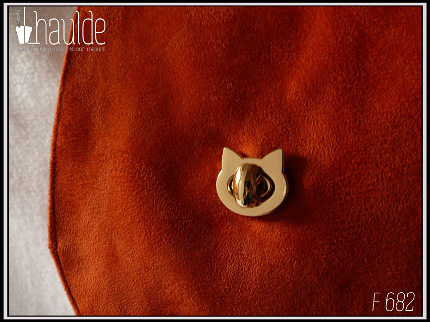 Vue de détail du fermoir tourniquet en forme de tête de chat en acier doré, sur la suédine orange foncé