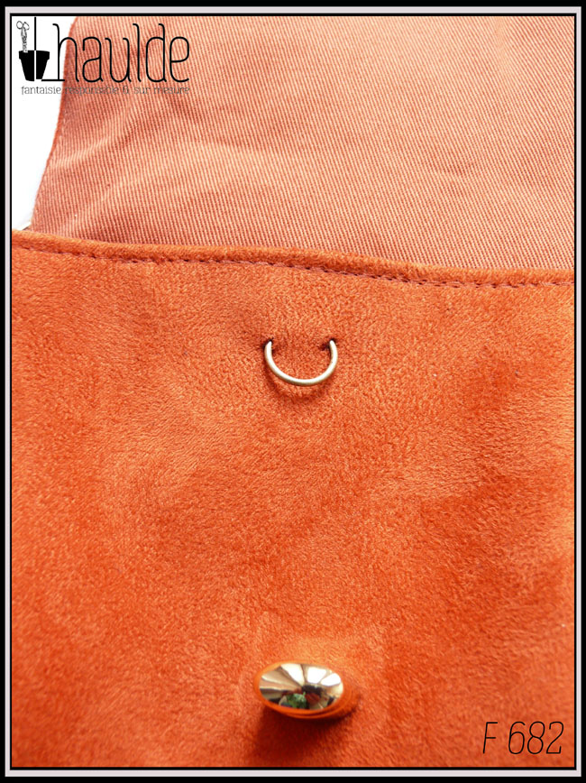 Vue de détail du devant du sac avec un "piercing" dans la suédine orange foncé, au-dessus du fermoir tourniquet. J'avais placé celui-ci beaucoup trop haut, j'ai fixé la suédine mais pour "cacher" les trous j'ai inséré un anneau doré