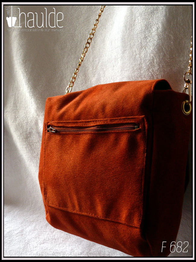 Vue de dos du sac avec sa poche extérieure zippée Sac à bandoulière à rabat en suédine orange foncé, bandoulière chaine et fermoir tourniquet en forme de tête de chat en acier doré.