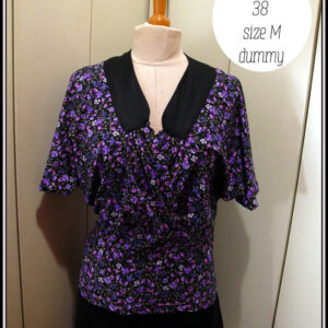 Haut en jersey noir imprimé petites fleurs violettes, encolure en V garni d'un col plat en satin noir, coeur croisé, manches chauve souris mi-longues, taille ajustée Vu de face sur un mannequin de couture taille 38