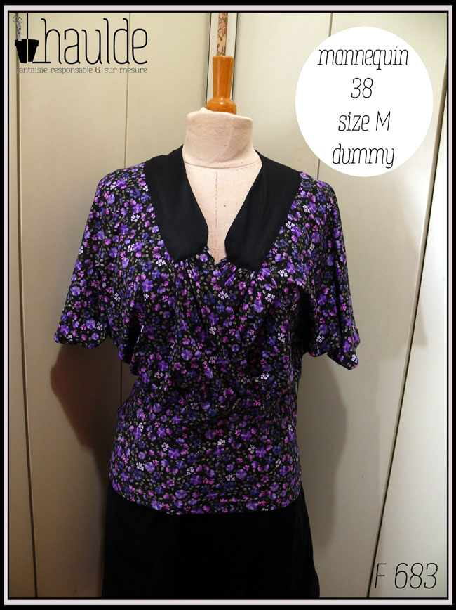 Haut en jersey noir imprimé petites fleurs violettes, encolure en V garni d'un col plat en satin noir, coeur croisé, manches chauve souris mi-longues, taille ajustée Vu de face sur un mannequin de couture taille 38