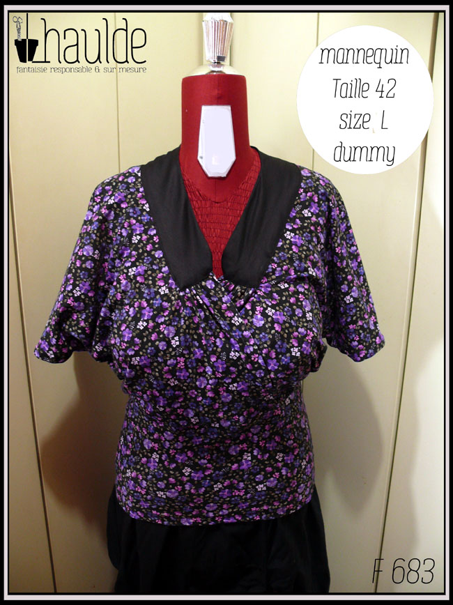 Haut en jersey noir imprimé petites fleurs violettes, encolure en V garni d'un col plat en satin noir, coeur croisé, manches chauve souris mi-longues, taille ajustée Vu de face sur un mannequin de couture taille 42