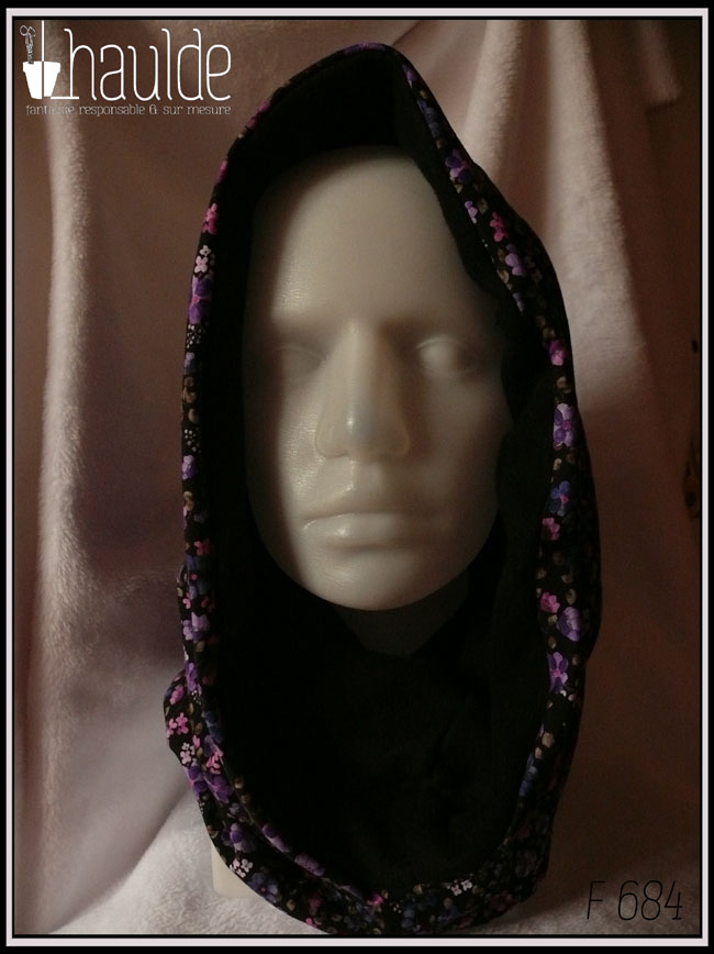 Tour de cou ample qui peut se porter en capuche, en jersey noir imprimé petites fleurs réalistes dans les tons violets doublé de polaire de coton noire Vu porté comme une capuche sur une tête de mannequin de face