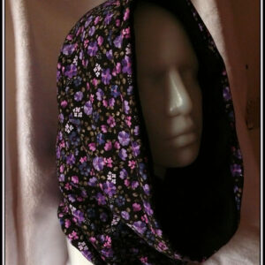 Tour de cou ample qui peut se porter en capuche, en jersey noir imprimé petites fleurs réalistes dans les tons violets doublé de polaire de coton noire Vu porté comme une capuche sur une tête de mannequin de trois quarts