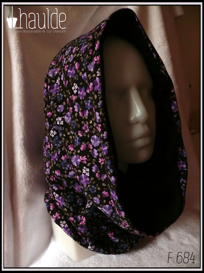Tour de cou ample qui peut se porter en capuche, en jersey noir imprimé petites fleurs réalistes dans les tons violets doublé de polaire de coton noire Vu porté comme une capuche sur une tête de mannequin de trois quarts